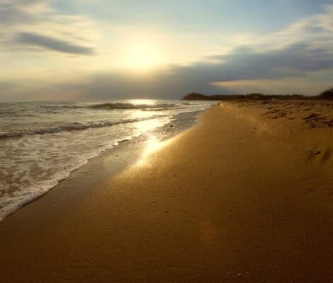 Złota plaża na Korfu o zachodzie słońca — spokojne fale Morza Jońskiego obmywające pusty brzeg, ciepłe światło słońca odbijające się na piasku, malowniczy i spokojny krajobraz.