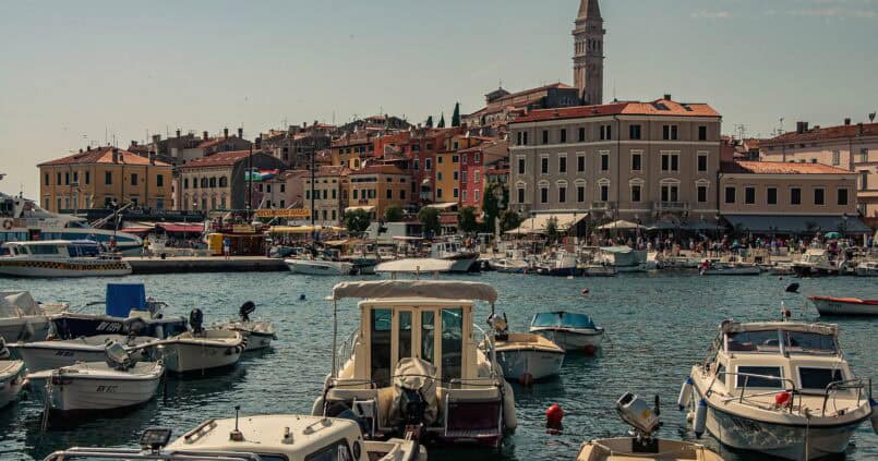 Widok z portu w Rovinj w Chorwacji — kolorowe fasady kamienic Starego Miasta odbijające się w spokojnej tafli Adriatyku, z charakterystyczną wieżą bazyliki św. Eufemii w tle.