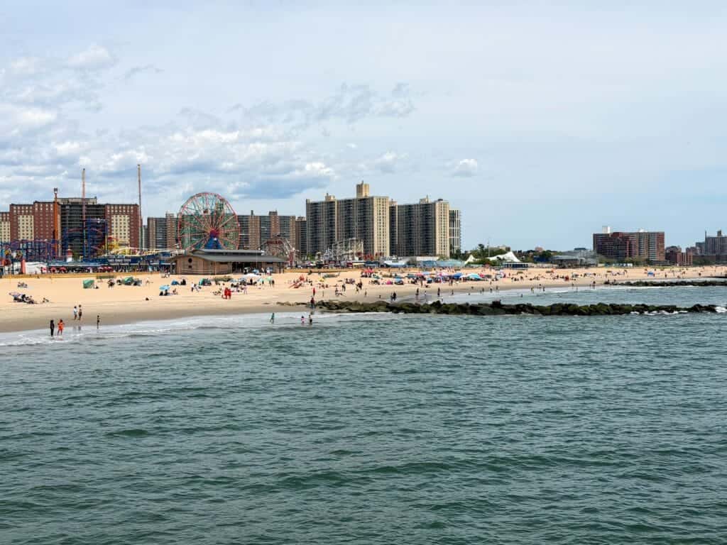 Panorama Coney Island widziana z molo w Nowym Jorku z plażą, oceanem i charakterystycznym lunaparkiem
